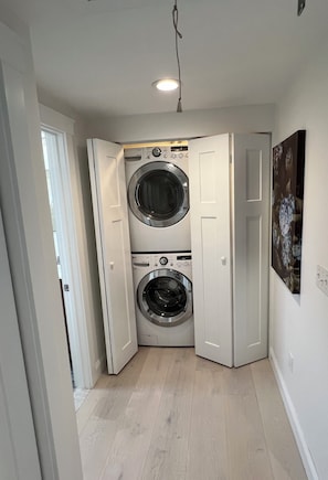 A laundry room with two stacked front-loading washing machines and a ceiling light. - Charming Waterfront Island Bungalow with DOCK in Narragansett! (Narragansett)