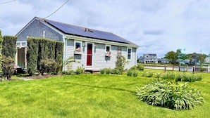 A single-story house with a red door, solar panels on the roof, and a well-maintained lawn. - Charming Waterfront Island Bungalow with DOCK in Narragansett! (Narragansett)