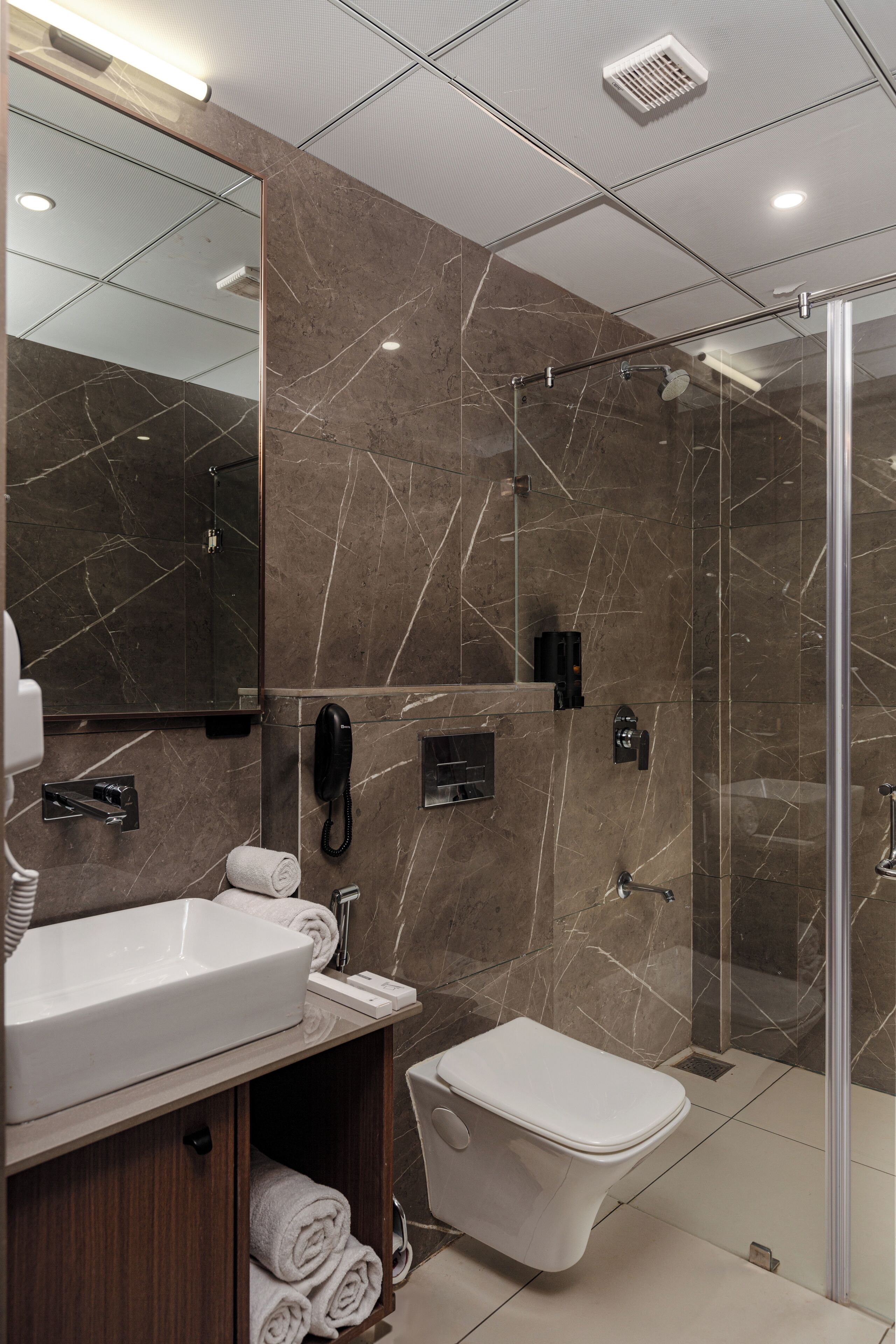 A modern bathroom with a large mirror, a sink, a toilet, and a glass shower enclosure.