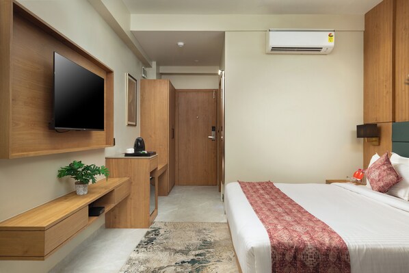 Una habitación de hotel moderna con una televisión de pantalla plana, un escritorio de madera, una cama con una manta estampada y un equipo de aire acondicionado.