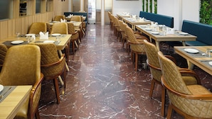 Une salle à manger spacieuse dotée d’un sol en marbre, de tables en bois et de chaises rembourrées.