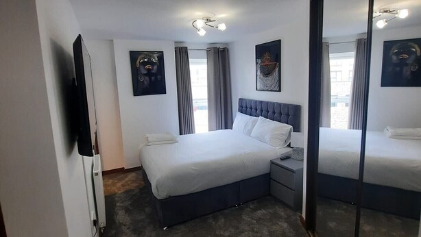 Habitación de hotel con una cama grande, una mesita de noche, un espejo y cuadros en las paredes.