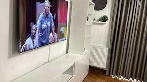 Una sala de estar moderna con un televisor de pantalla plana montado en la pared, un mueble blanco para equipo multimedia, un radiador y una ventana con cortinas.