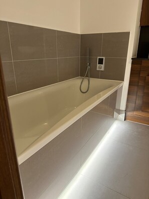 Ein modernes Badezimmer mit freistehender Badewanne, Duschbrausehandstück und einer Wandbedienung.