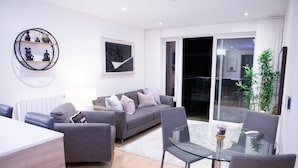 Un salon moderne avec un canapé gris, une table basse en verre et un coin repas comprenant une table et des chaises en verre.