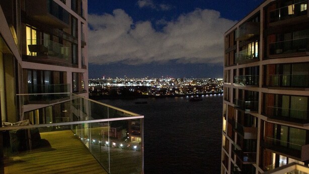 Une vue nocturne prise depuis un immeuble de grande hauteur, donnant sur un paysage urbain et une étendue d’eau.