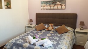 A neatly made bed with floral bedding, two brown pillows, a teddy bear, and towels with flowers. - Casa Tua sul tetto di Roma (Rome)