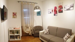 A living room with a sofa, a chair, a bookshelf, a floor lamp, and a TV. - Casa Tua sul tetto di Roma (Rome)