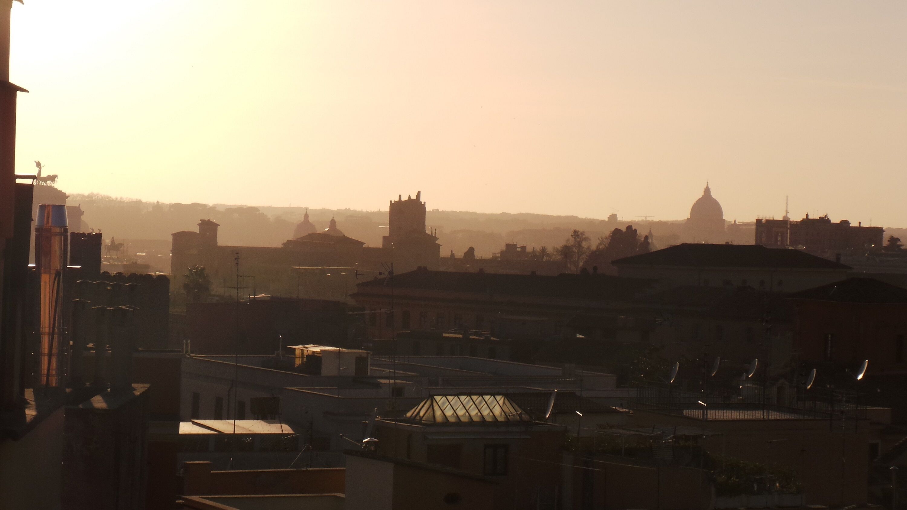 Une vue sur une ville au coucher du soleil, avec des bâtiments imposants et une structure en forme de dôme visible au loin.