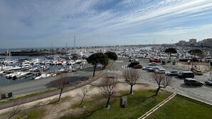 Ein Yachthafen mit zahlreichen angestückten Booten, ein Parkplatz mit Autos und einem wolkenlosen Himmel.