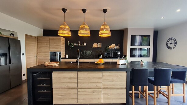 A modern kitchen with a large island, wooden cabinets, and pendant lighting.
