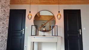 A hallway with two black doors, a wooden ceiling, a round mirror, and two wall-mounted light fixtures.