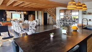 A spacious dining area with a long wooden table and chairs, a kitchen with modern appliances, and a staircase leading to an upper level.
