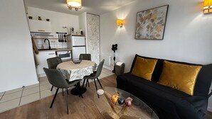 A compact living space with a dining area, kitchenette, and a sofa with gold cushions. - Renovated T2 with WiFi and parking 200m from the Spa (La Roche-Posay)