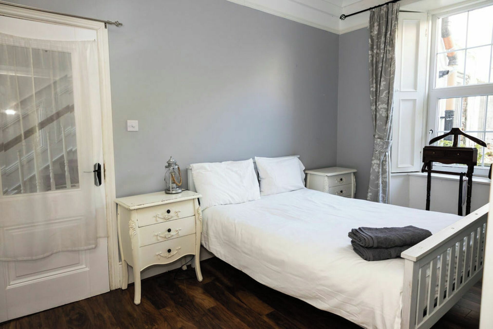 A bedroom with a bed, white nightstands, a dresser, a hanging light, and a window with curtains.