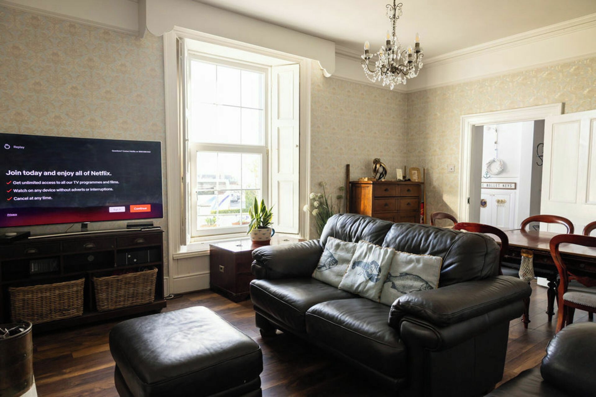 A living room with a leather sofa, a television, a chandelier, and a dining area.