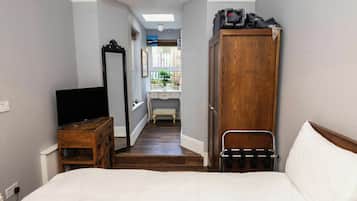 A bedroom with a bed, a wooden wardrobe, a television on a wooden dresser, and a hallway leading to a bathroom.