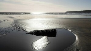 A beach with a large rock in the water, waves, and a distant cliff. - Beach Views, Elegant & Modernised 5BD Period Home (Tramore)