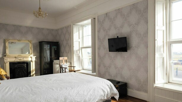 A bedroom with a large bed, a fireplace, a television, and large windows. - Beach Views, Elegant & Modernised 5BD Period Home (Tramore)