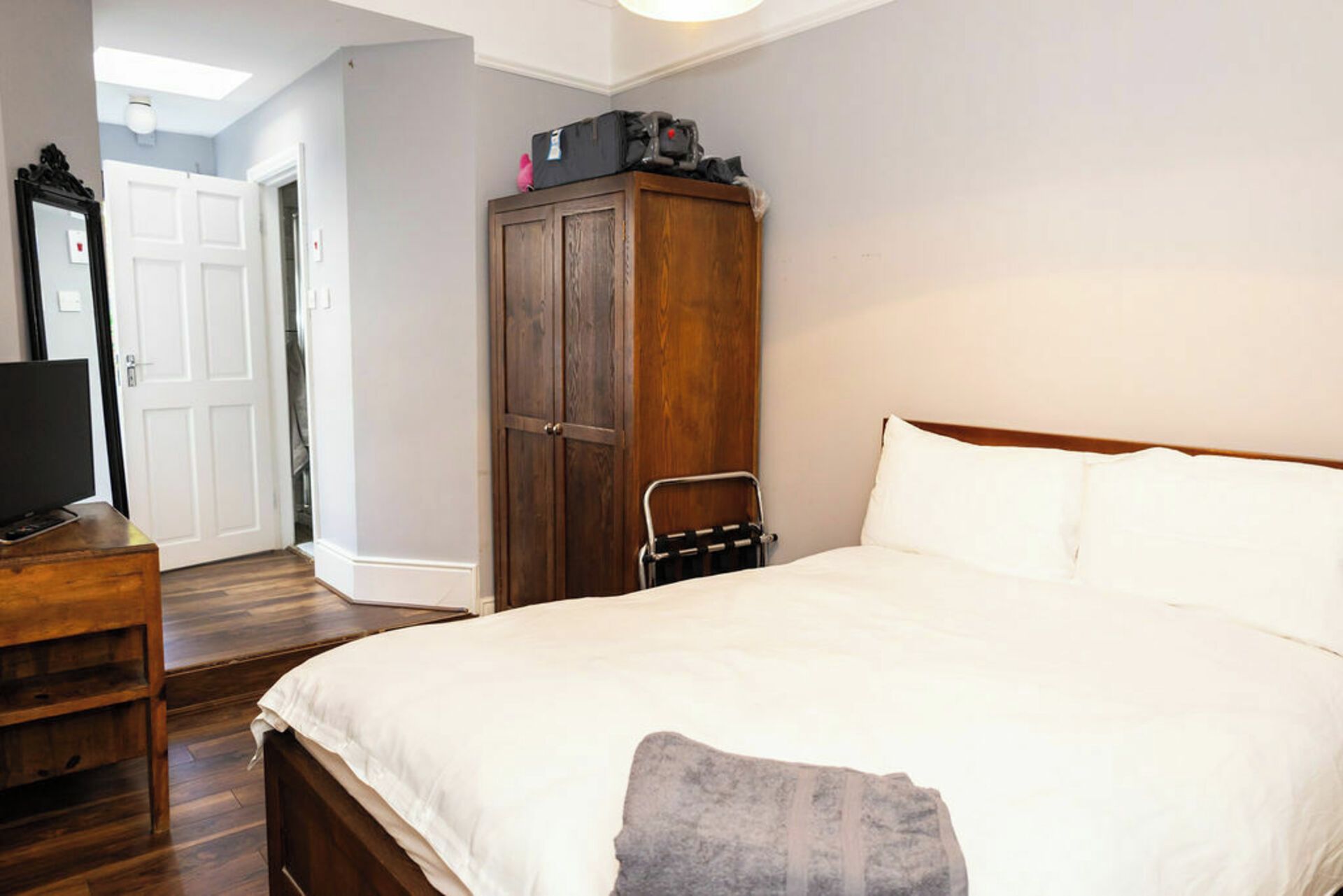A bedroom with a wooden wardrobe, a bed with white linens, a wooden nightstand, and a television on the left.