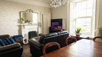 A living room with a fireplace, a television, a chandelier, and a dining table.