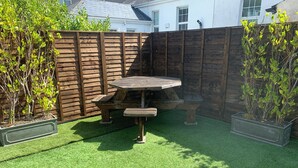 A backyard with a wooden table and benches, surrounded by a wooden fence and green artificial grass. - Beach Views, Elegant & Modernised 5BD Period Home (Tramore)