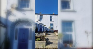 A white building with a symmetrical facade, a central entrance with a door, and a staircase leading to the entrance.
