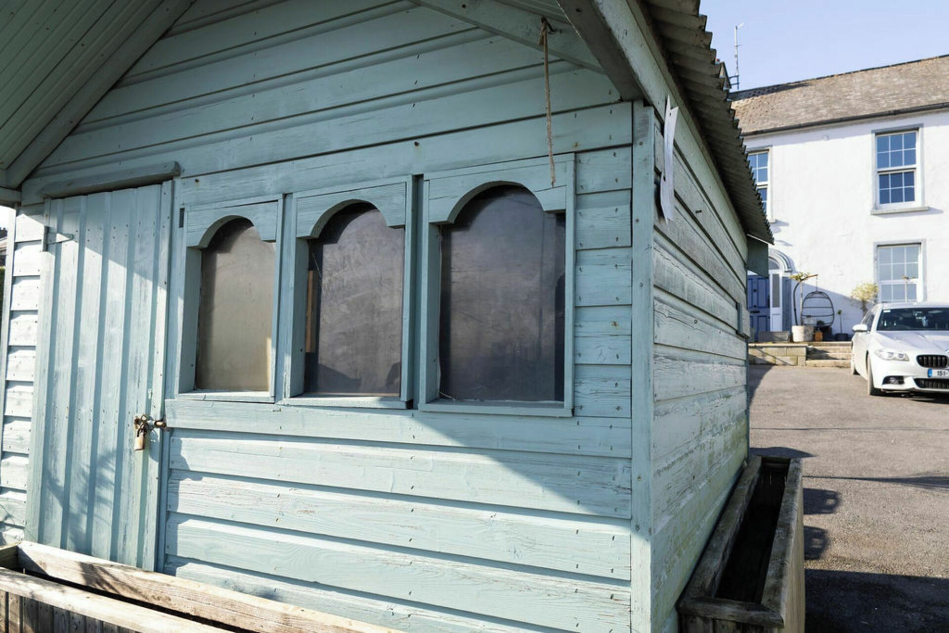 A light blue wooden building with three arched windows and a door.