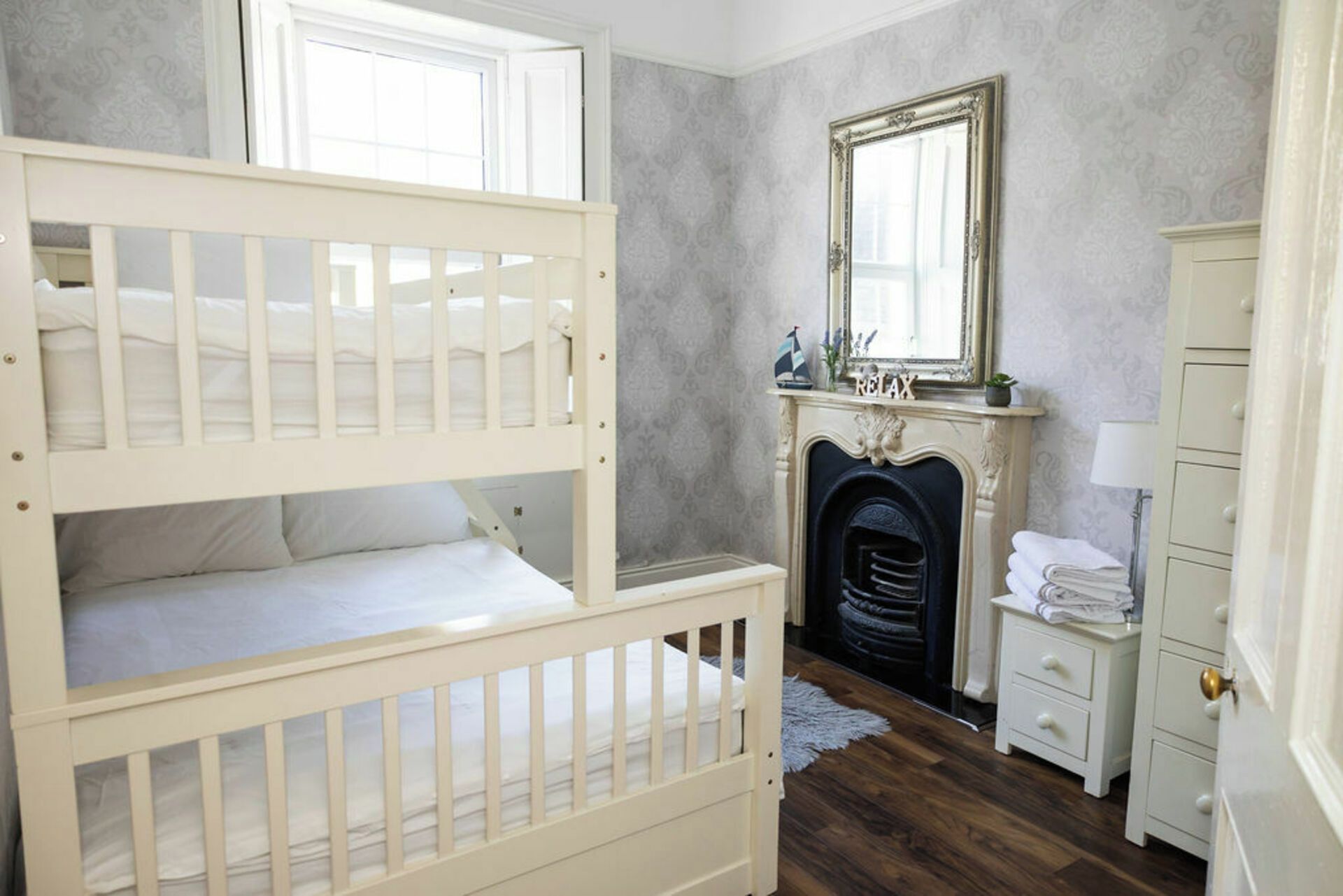 A bedroom with a bunk bed, a fireplace, a mirror, and a dresser.