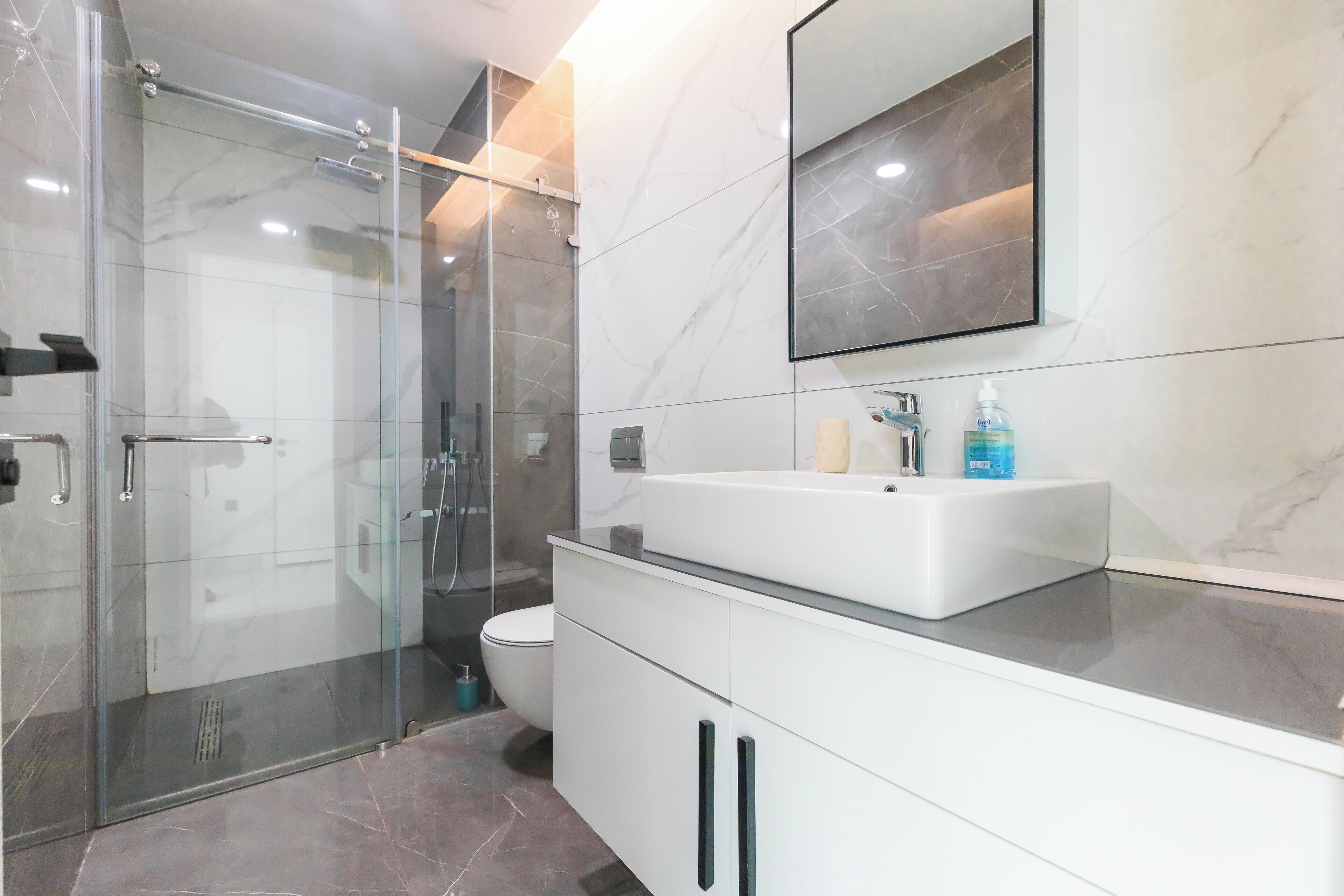 A modern bathroom with a glass shower enclosure, a white sink, and a large mirror.