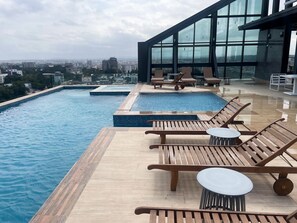 Ein Rooftop-Endlospool mit Holzliegen und -tischen, umgeben von Glaswänden mit Blick auf die Stadt.