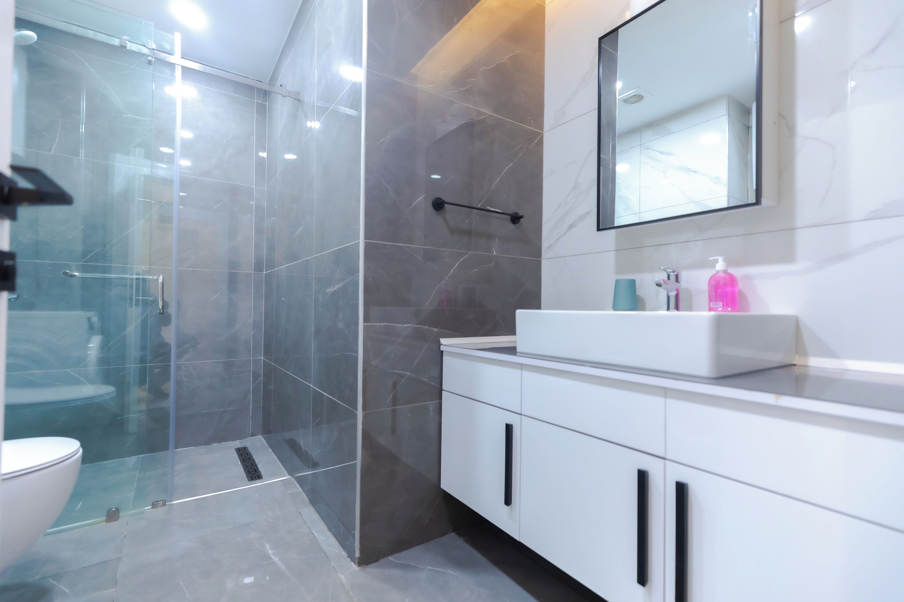 Un baño moderno con ducha de vidrio, tocador blanco con espejo y un inodoro.