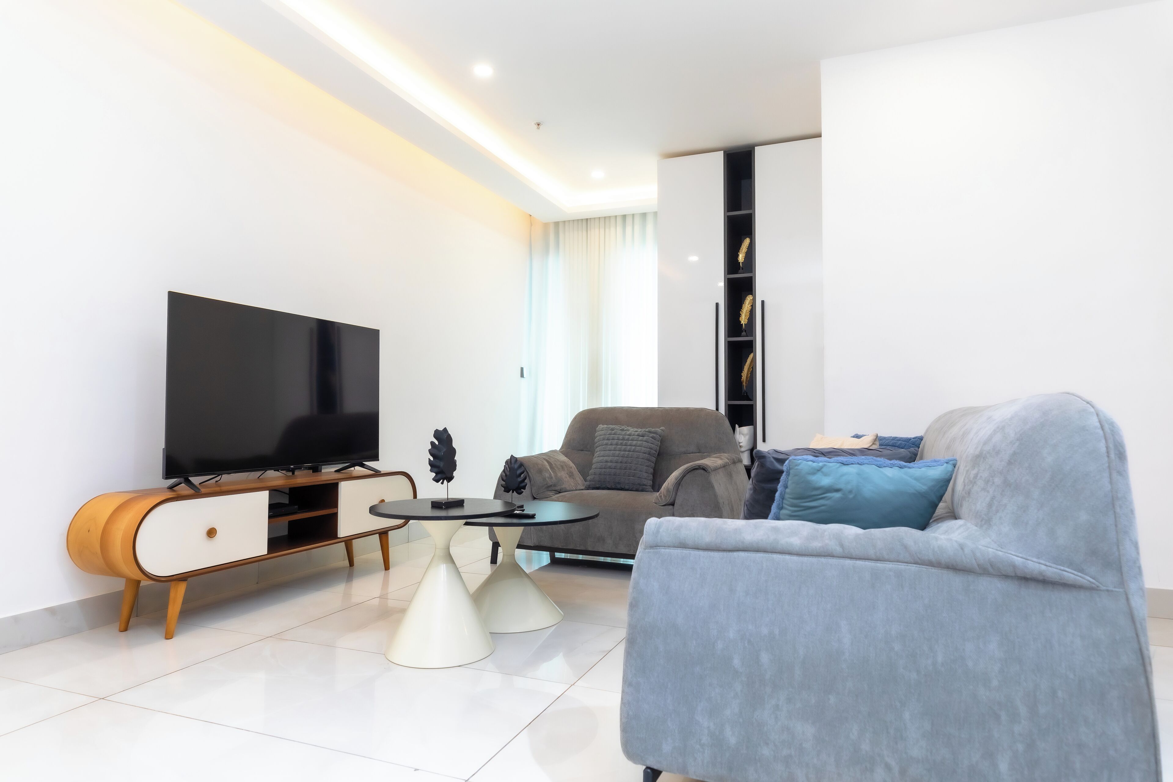 A modern living room with a flat-screen TV, a sofa, a coffee table, and a cabinet with decorative items.