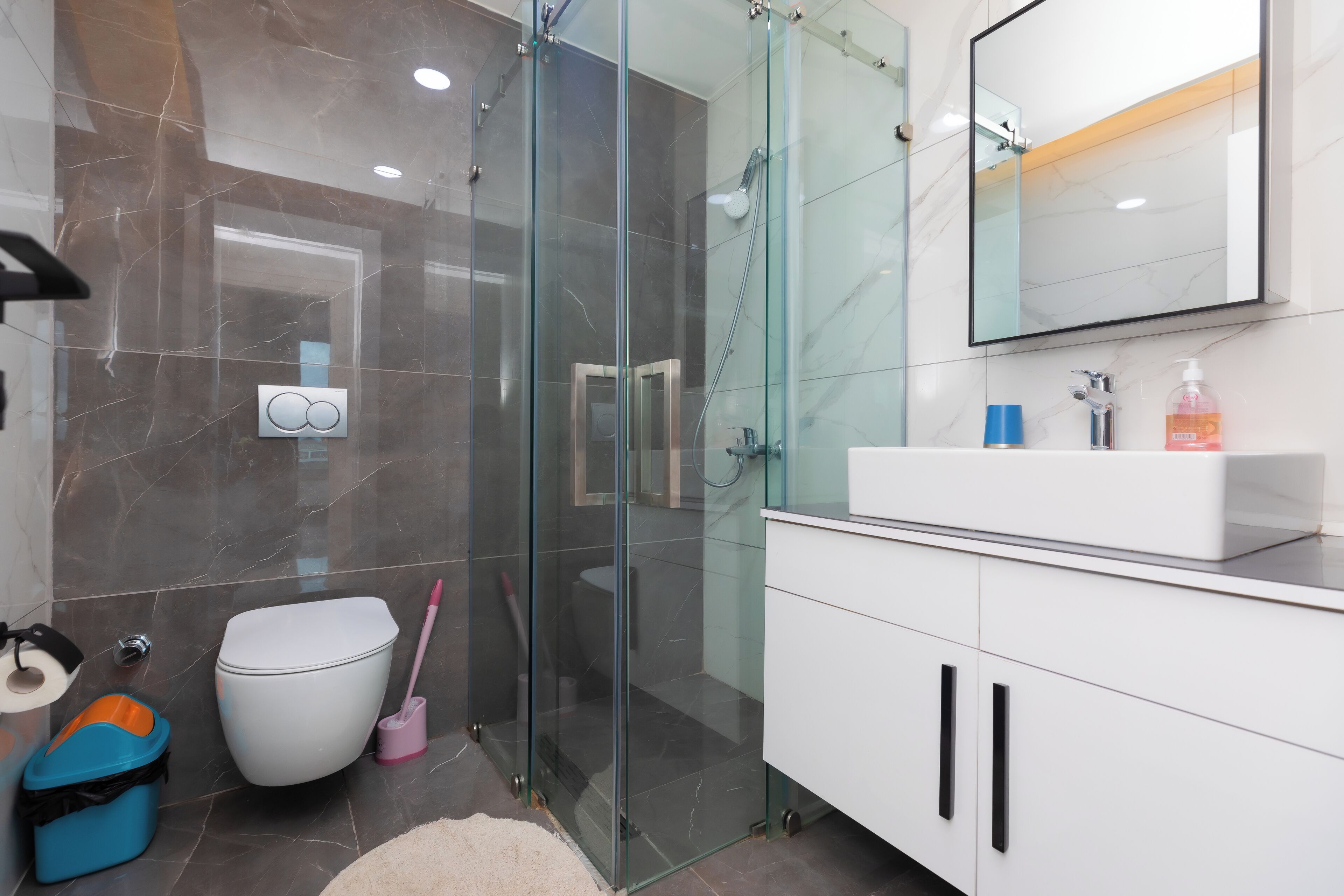 A modern bathroom with a glass-enclosed shower, a white toilet, and a white sink with a mirror above it.