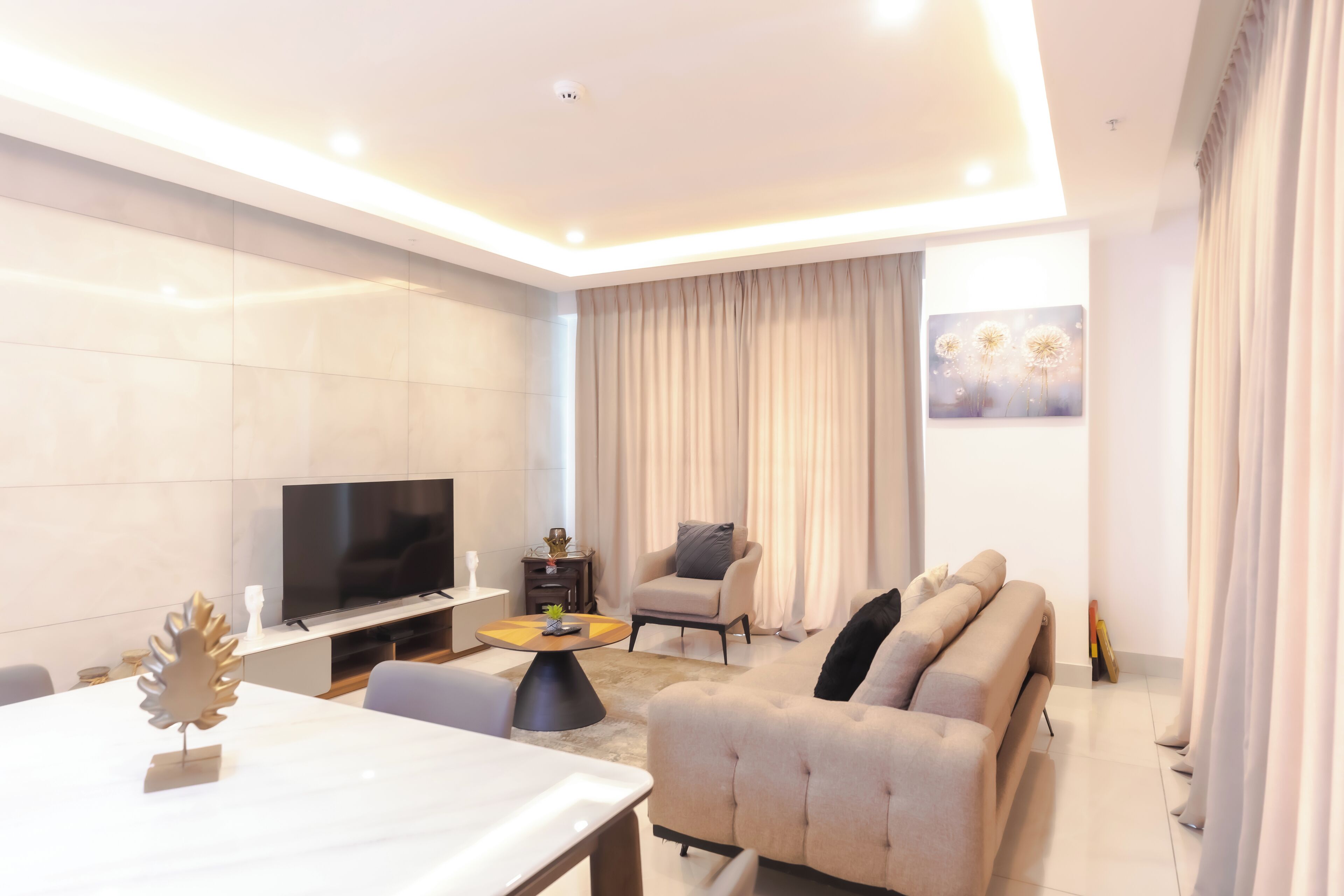 A modern living room with a flat-screen TV, a sofa, a coffee table, and a dining area.