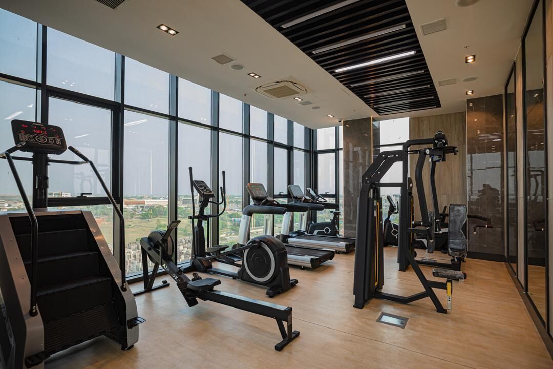 Une salle de sport moderne équipée de divers appareils d’exercice, dotée de grandes fenêtres et offrant une vue sur la ville.