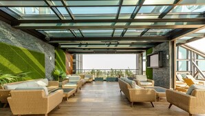 A rooftop lounge with wicker furniture, a glass ceiling, and a view of the city. - Kass Towers (Accra)