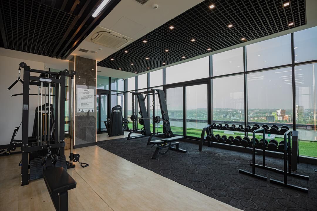 A gym with various exercise equipment, large windows, and a view of a cityscape.
