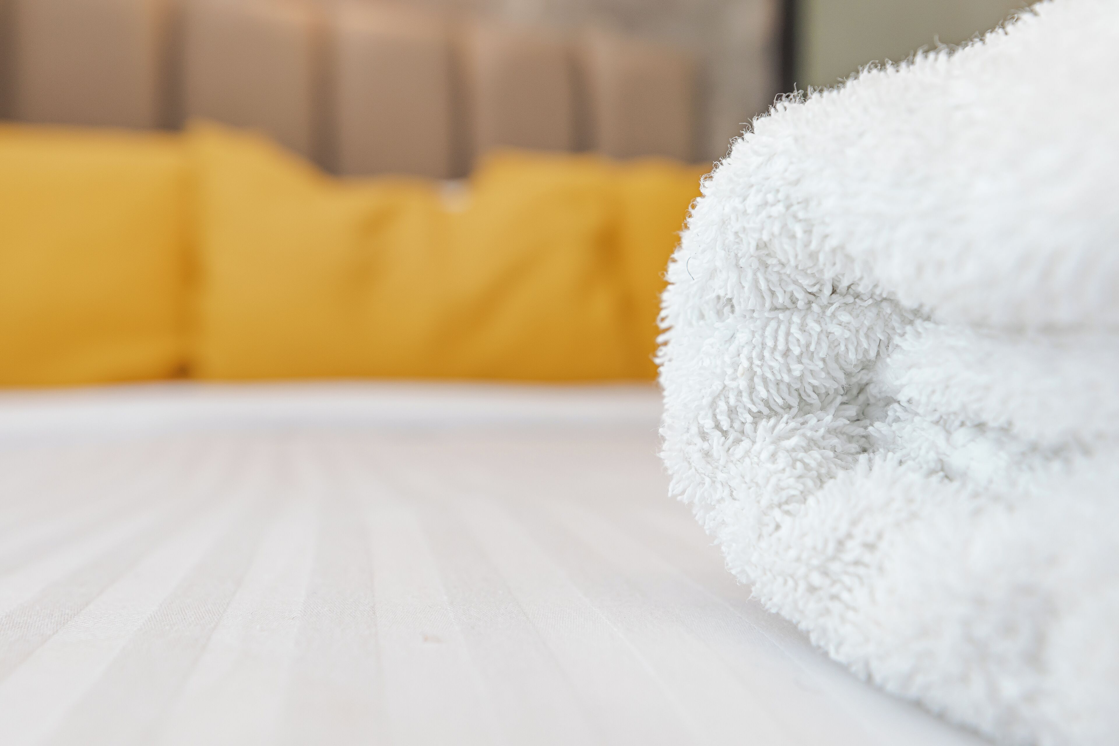 A white fluffy towel on a wooden surface with a blurred yellow background.