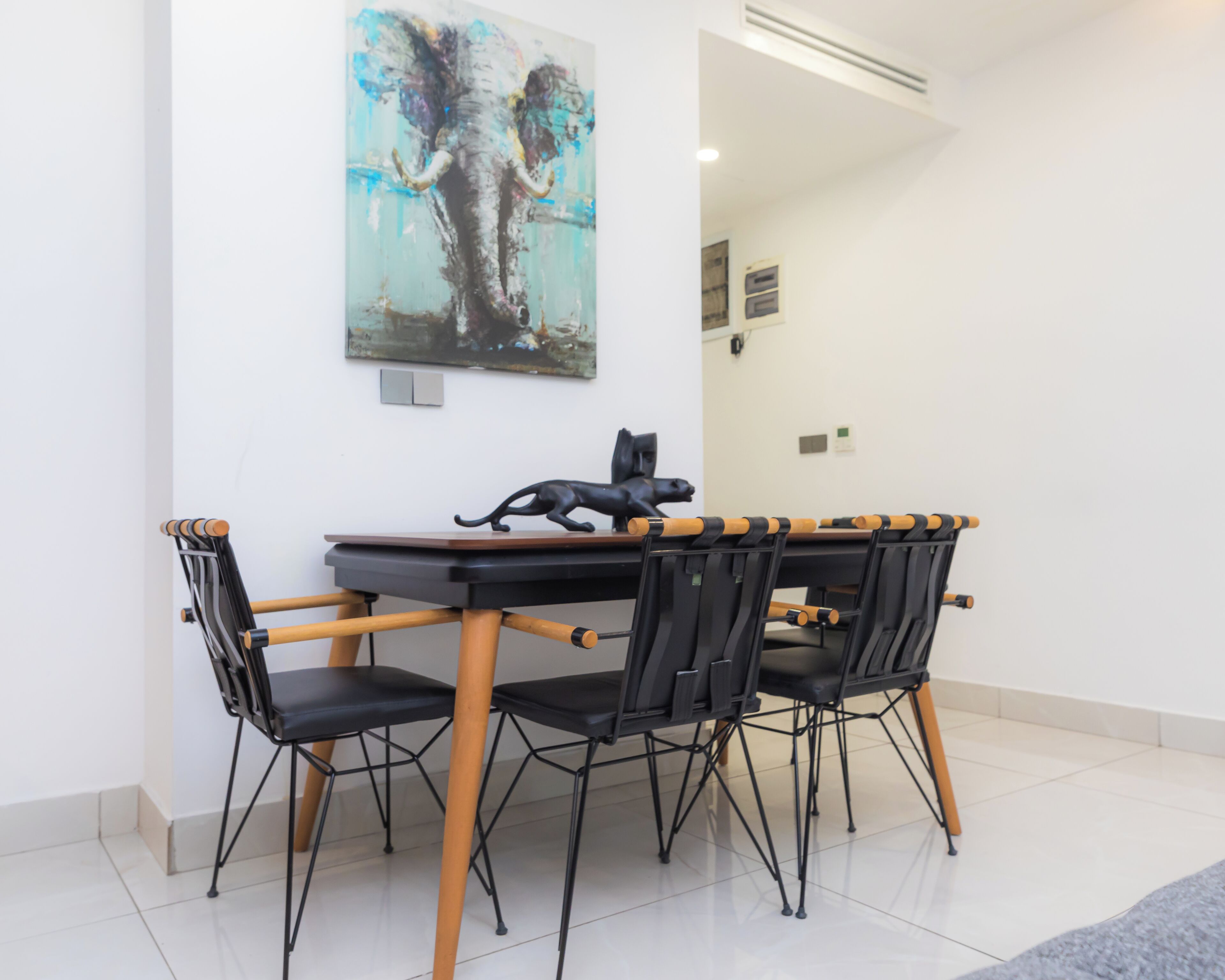 A dining area with a table and chairs, a painting on the wall, and a small sculpture on the table.