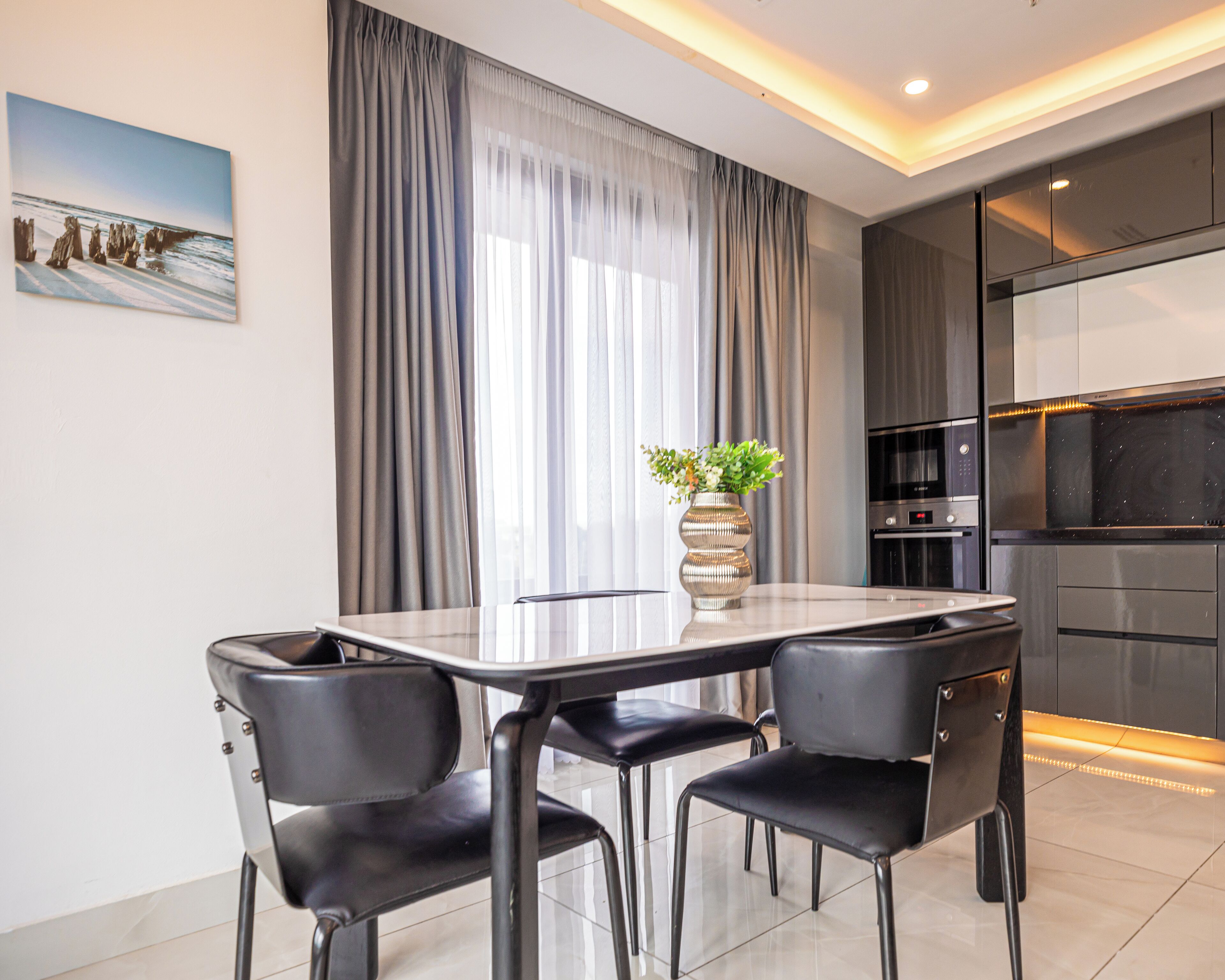 A modern dining area with a glass table, black chairs, and a vase with flowers.