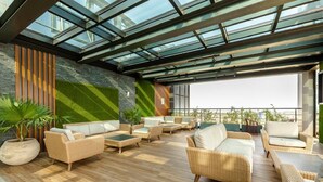 A rooftop lounge with wicker furniture, a glass ceiling, and a view of the cityscape. - Kass Towers (Accra)