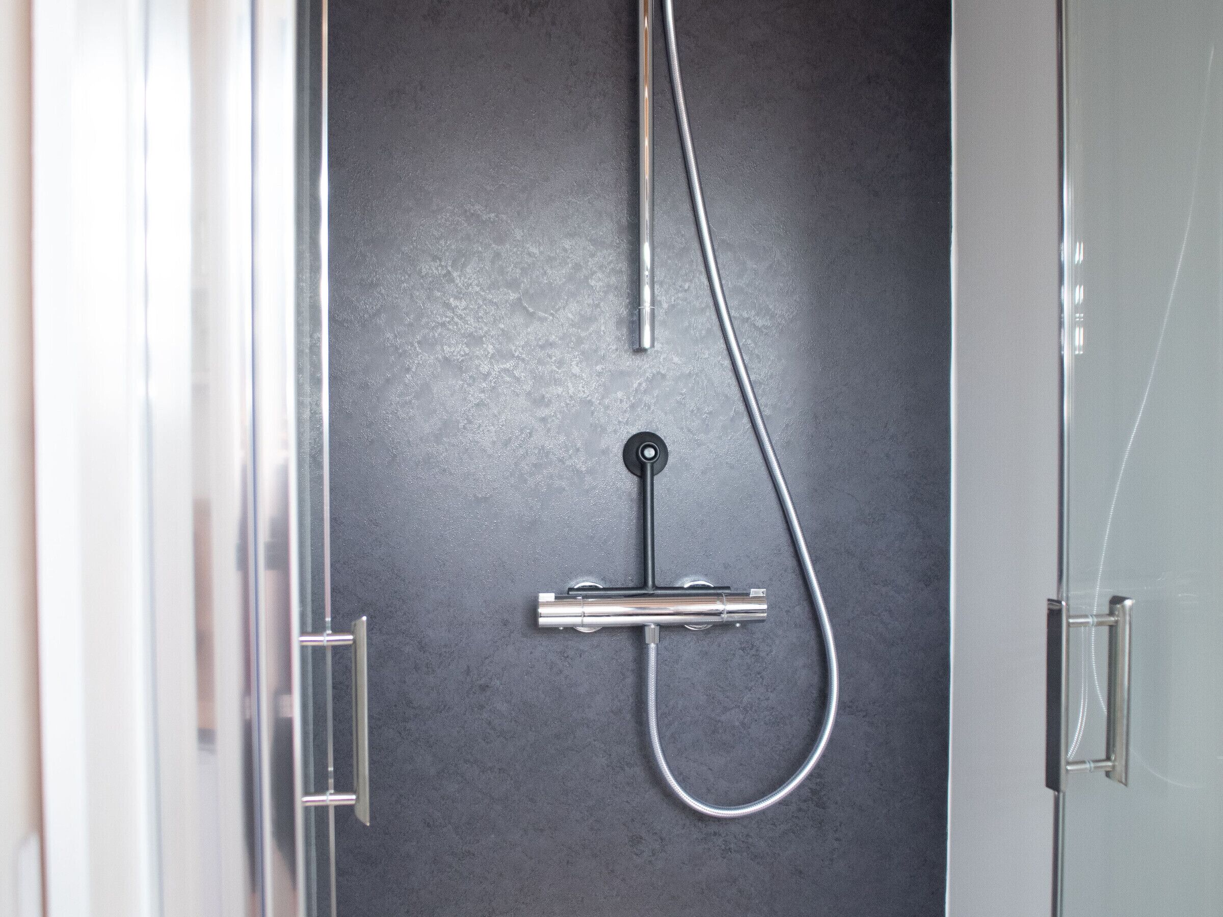 Eine moderne Dusche mit elegantem Design, einer Bedienkonsole und einem flexiblen Schlauch.