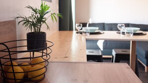 Un coin repas avec une table en bois, une plante en pot et un panier rempli d’oranges.