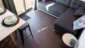 Un salon moderne avec un canapé gris foncé, une table à manger en bois sur laquelle sont disposés des assiettes et des couverts, et une petite table ronde agrémentée d’un objet décoratif.