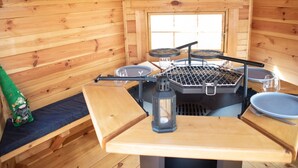 L’intérieur d’un chalet en bois, avec un barbecue, un coin salon et une fenêtre.