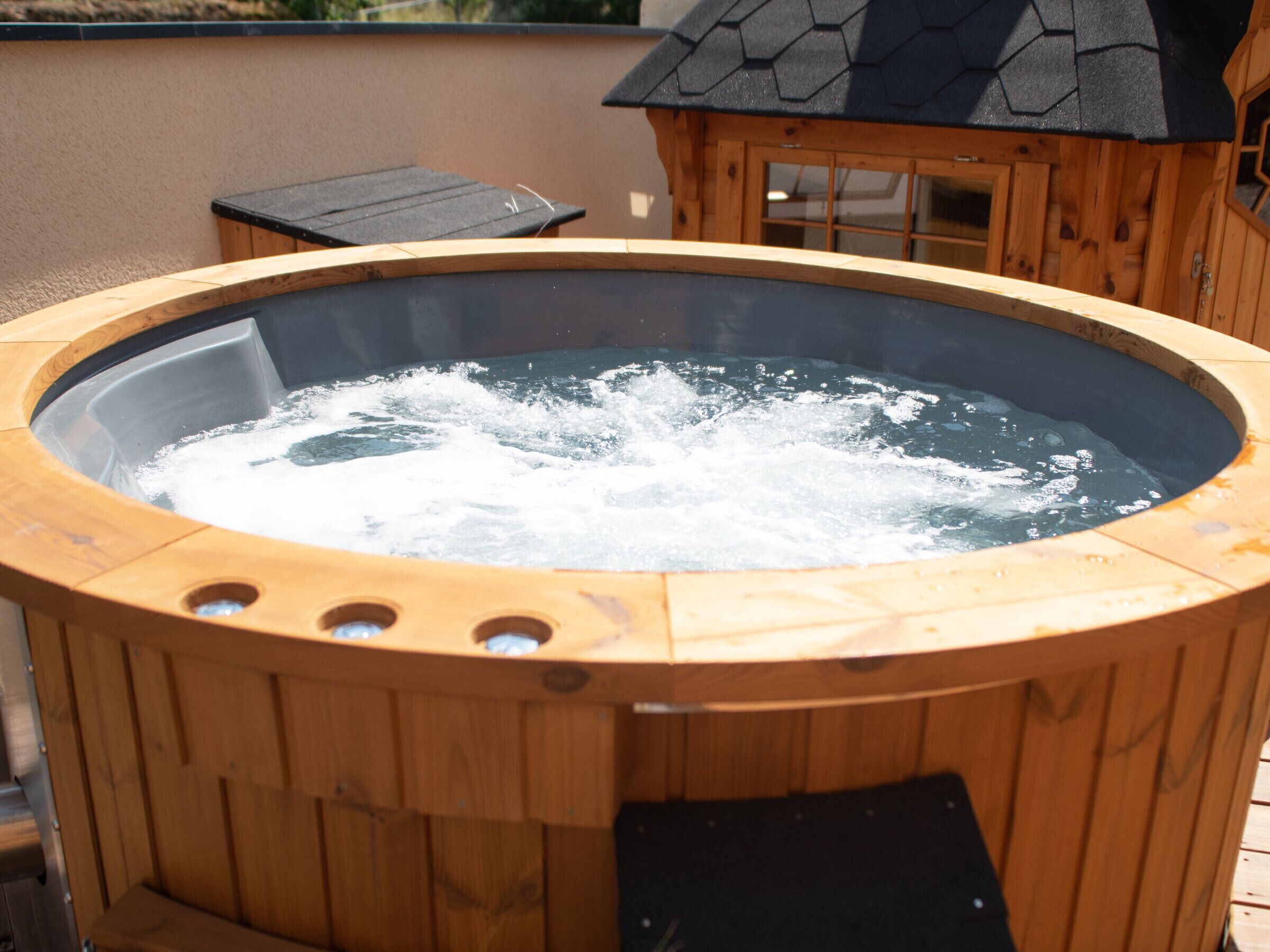 A wooden hot tub with a black roof and a wooden deck surrounding it.