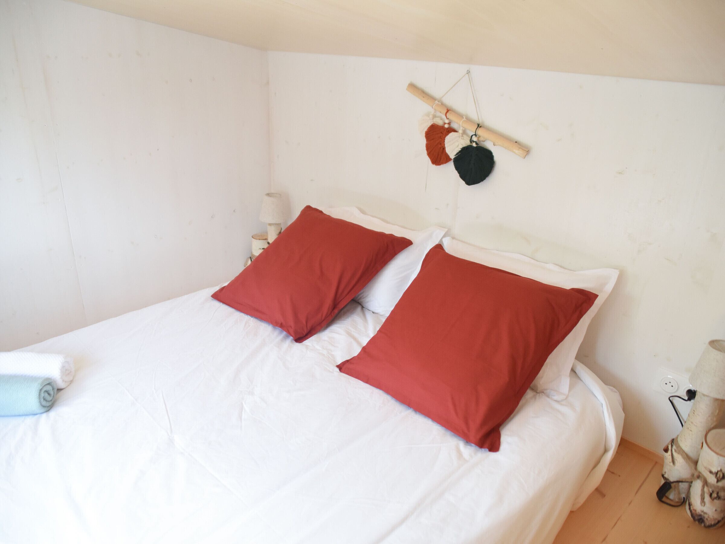 A bed with white bedding and two red pillows, a wooden headboard, and a wall-mounted hanging with a red and black object.