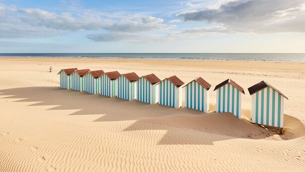 Une plage bordée d’une rangée de cabanes de plage à rayures.