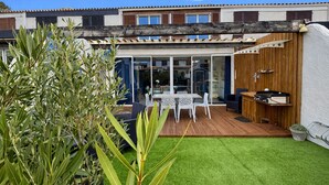 Un espace patio avec une terrasse en bois, une table et des chaises, ainsi qu’un barbecue.